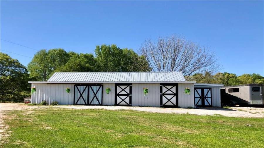 Front of barn shows 2 of the matted stalls, tack room is to the left of the sliding door when open allows nice cross breeze but makes feed delivery easy and the sliding doors to the far right is for hay/shavings delivery and storage. Trailer parking location makes it convenient to load up and go.