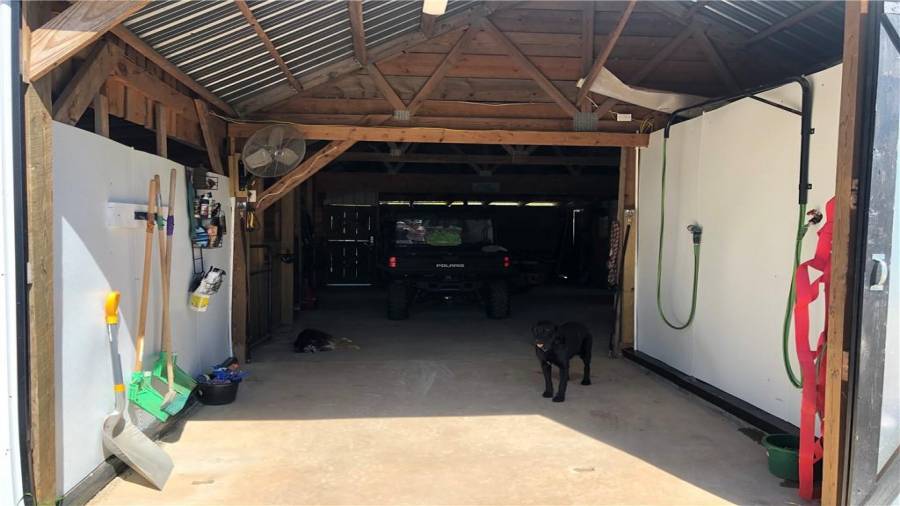 Wash stall area from the entry door. Hot water supplied by the overhead boom and an electric tankless water heater the is in the feed room for protection during the cold winter nights. Cold water is available from a separate hose. An aisle guard can be used if open grazing is allowed to keep horses out of the barn.