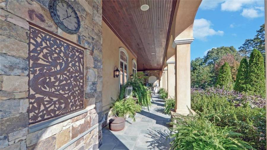 A covered walkway spans the exterior of the home with access to the pool area and gardens.