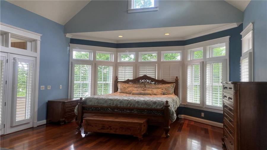 The blue room is a private en-suite. Picture perfect spacious bedroom on the upper level. Just a wall of windows on two sides. Plantation shutters y are very nice to let the natural light come in when you want.  The brazil hardwood flooring is excellent condition and just beautiful. Did you notice the trey ceiling with lighting over the bed and the dormer windows above the windows? What a spacious bedroom with built in closet shelving. Private balcony off this bedroom overlooks lake and mountains.