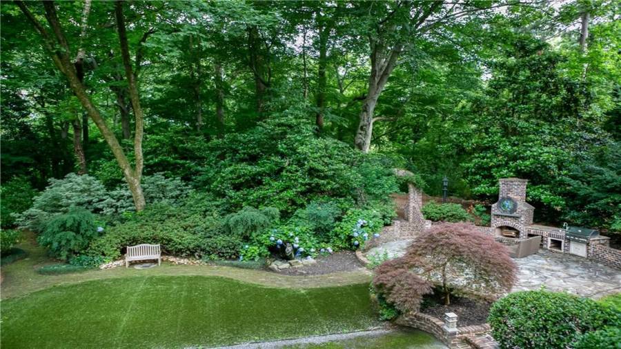 View of back yard from porch. See the stone water feature, stone patio, outdoor kitchen, and undisturbed private neighborhood land behind.