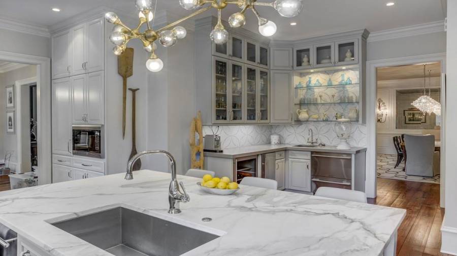 Kitchen island has sink, nickle faucet, and is Calacatta Gold marble. See wet bar in view with wine cooler, dishwasher drawers, open shelving, and glass front cabinets for decorate barware.