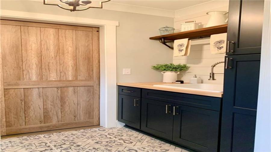 Pocket door off kitchen leads to spacious laundry room with navy blue cabinets, including 2nd pantry, Shiplap wall, custom wood shelf with rod, & wood countertop. Extra-deep sink and pull-down faucet!