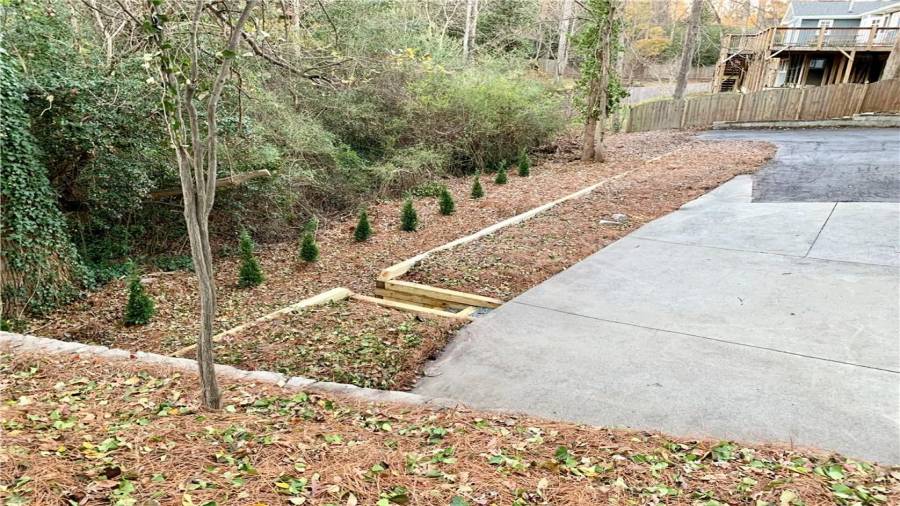 Newly constructed retaining wall with staircase down to natural area & creek. Straight line of Leland cypress will grow to provide so much privacy!