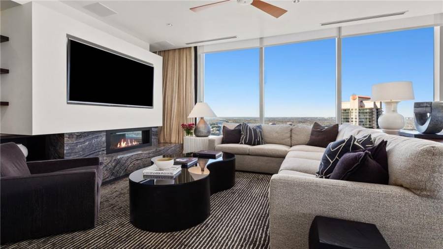 The Sunset and Buckhead Skyline Facing Den is 17 x 29 and Offers Stunning Views Of Buckhead and Midtown. Note Two Seating Areas and The Natural Gas Fireplace And Built-In Television Panel and Custom Built-Ins To The Left Of The Television. The Kitchen Opens to This Space for A Casual Family Lifestyle And Effortless Entertaining.